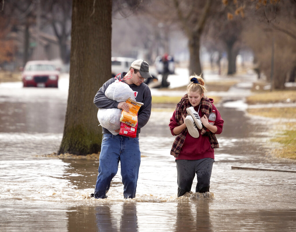 Anthony Thomson, left, and Melody Walton make their way out of a flooded neighborhood Sunday, March 17, 2019, in Fremont, Neb. (AP)
