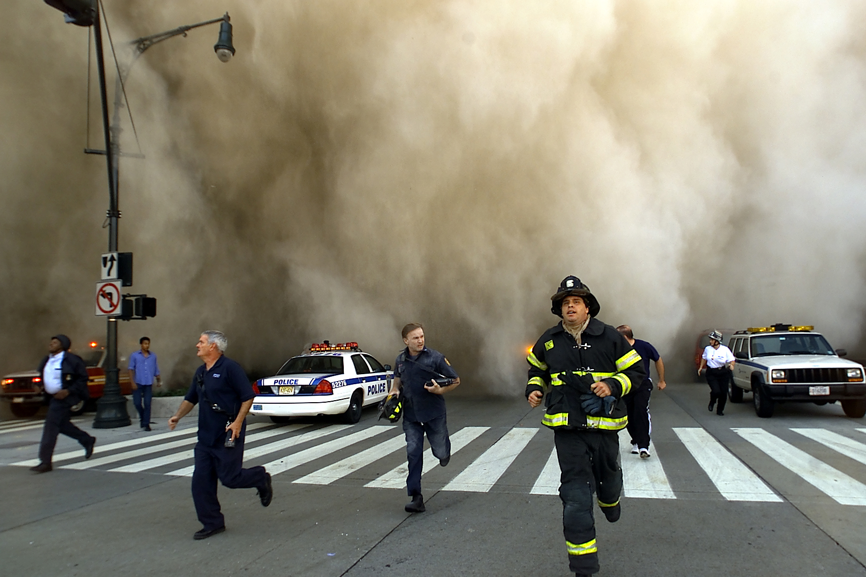 Policemen and firemen run from the huge dust cloud caused by World Trade Center's Tower One collapse after terrorists crashed two hijacked planes into the twin towers, September 11, 2001, in New York City (Source: Getty Images)