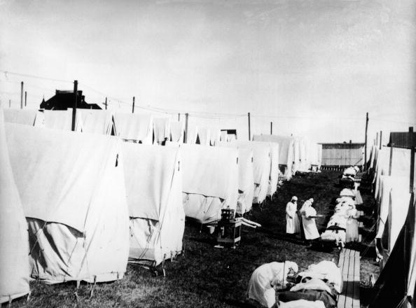 Masked doctors and nurses treat flu patients lying on cots and in outdoor tents at a hospital camp during the influenza epidemic of 1918 (Getty Images)