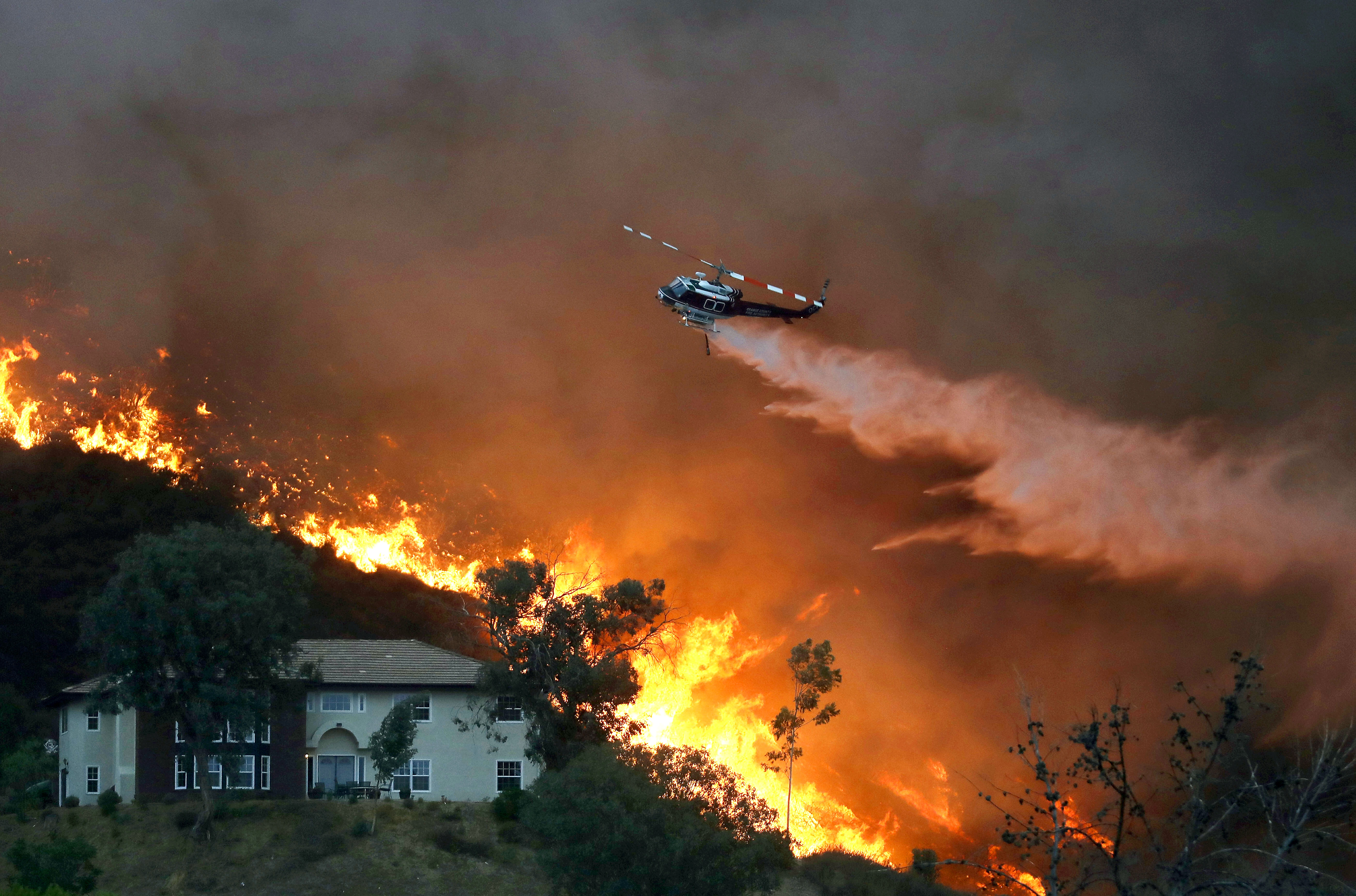 A firefighting helicopter makes a water drop as the Holy Fire burns near homes on August 9, 2018 in Lake Elsinore, California. The fire continues to grow amidst a heat wave and has now burned 10,236 acres while remaining just five percent contained.