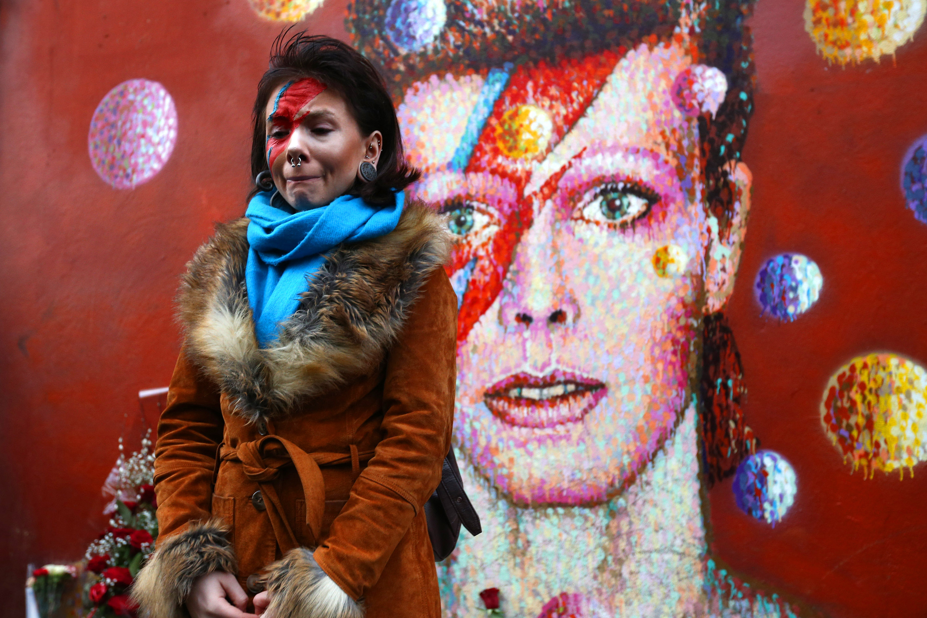 David Bowie fan Rosie Lowery pauses after laying flowers at his mural in Brixton on January 11, 2016 in London, England. British music and fashion icon David Bowie died earlier today at the age of 69 after a battle with cancer. Source: Getty